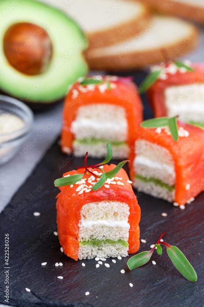 Mini sandwiches with smoked (salted) salmon or trout, avocado, cream cheese, sesame seeds and micro-greens on white bread. A delicious snack. Canapes. Tapas. Breakfast. Selective Focus Mini sandwiches with smoked (salted) salmon or trout, avocado, cream cheese, sesame seeds and micro-greens on white bread. A delicious snack. Canapes. Tapas. Breakfast. Selective Focus