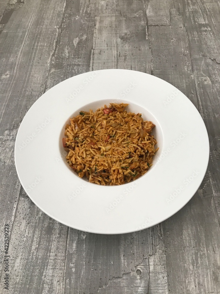 A bowl of chicken tikka biryani against a wooden background A bowl of chicken tikka biryani against a wooden background