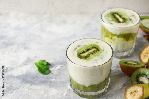 Yogurt with kiwi in a glass. Fruit and berry smoothie. Milkshake with kiwi and banana. Healthy eating. Light background. Copy space.