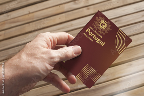 A hand holds a Portuguese passport and a wooden board in the background, copy space