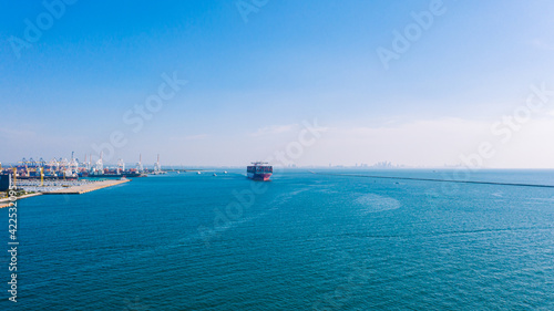 Billede på lærred Container ship approaching port city, surrounded by vast blue sea, highlighting logistics, import-export business, and maritime economy