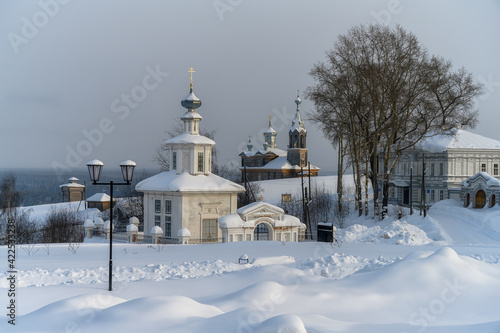 View of the ancient city of Cherdyn (Northern Urals, Russia) on a frosty winter day. Ancient wooden churches with domes rise above the deep snowy field. In the distance under the mountain river valley