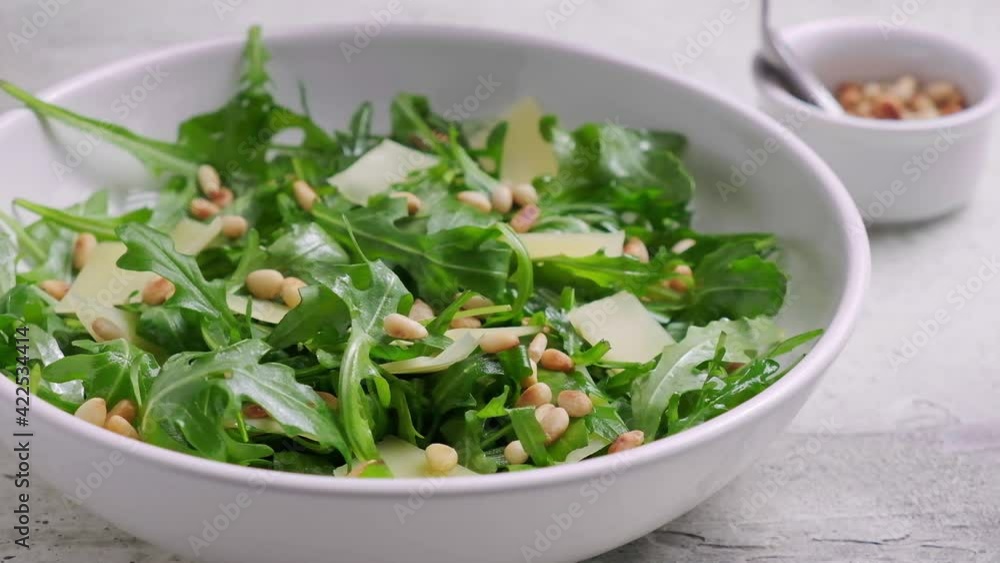 Arugula and parmesan salad with pine nuts in white bowl. Italian cuisine concept. Arugula and parmesan salad with pine nuts in white bowl. Italian cuisine concept.