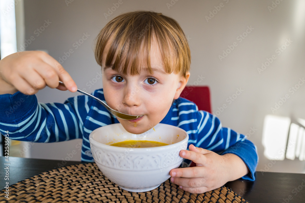 Cute little child having lunch at home. Toddler sitting at the table, tasting soup in a bowl. Happy smiling boy eating healthy domestic food. Cute little child having lunch at home. Toddler sitting at the table, tasting soup in a bowl. Happy smiling boy eating healthy domestic food.