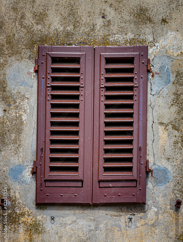 Antique plastered wall with red shutters in Panzano, Italy