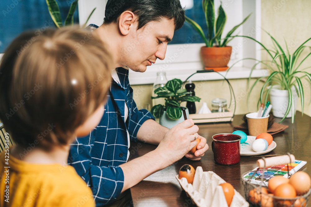 Easter day. Father and son painting eggs on wooden background. Family sitting in a kitchen. Preparing for Easter, creative homemade decoration. Easter day. Father and son painting eggs on wooden background. Family sitting in a kitchen. Preparing for Easter, creative homemade decoration.