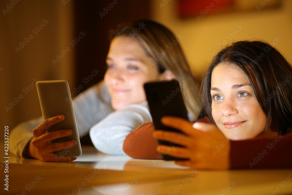 Two roommates using her smart phones in the night Two roommates using her smart phones in the night