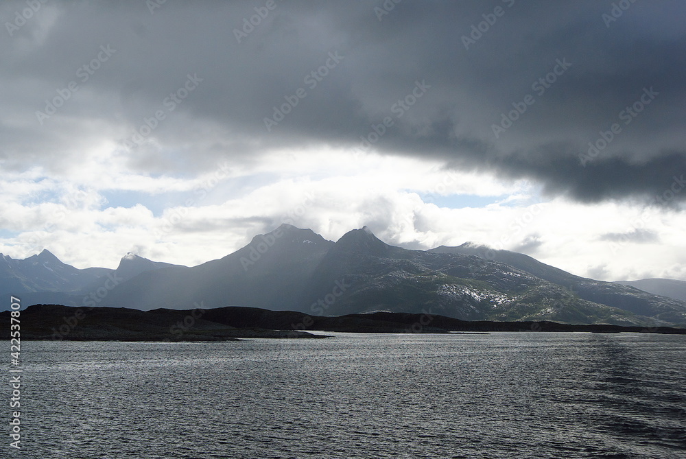 View from ferry to the grey and rainy clouds over the mountains of Helgeland archipelago in the Norwegian sea. Boat water trail on the water