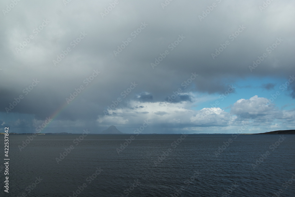 Rainbow in the grey and rainy clouds over the mountains of Helgeland archipelago in the Norwegian sea