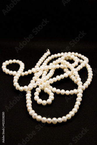 Long white pearl beads lie on a black background