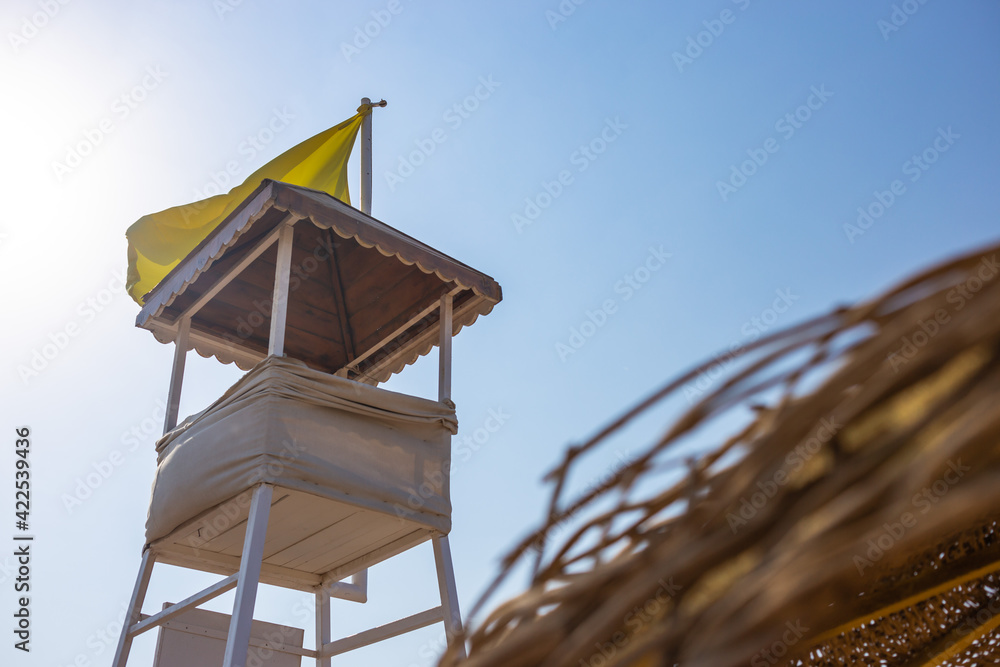 White, wooden empty rescue tower on the desolate beach near the sea with yellow warning flag White, wooden empty rescue tower on the desolate beach near the sea with yellow warning flag