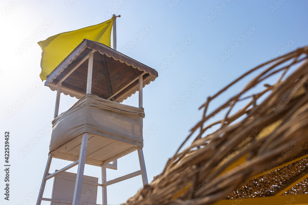 White, wooden empty rescue tower on the desolate beach near the sea with yellow warning flag White, wooden empty rescue tower on the desolate beach near the sea with yellow warning flag