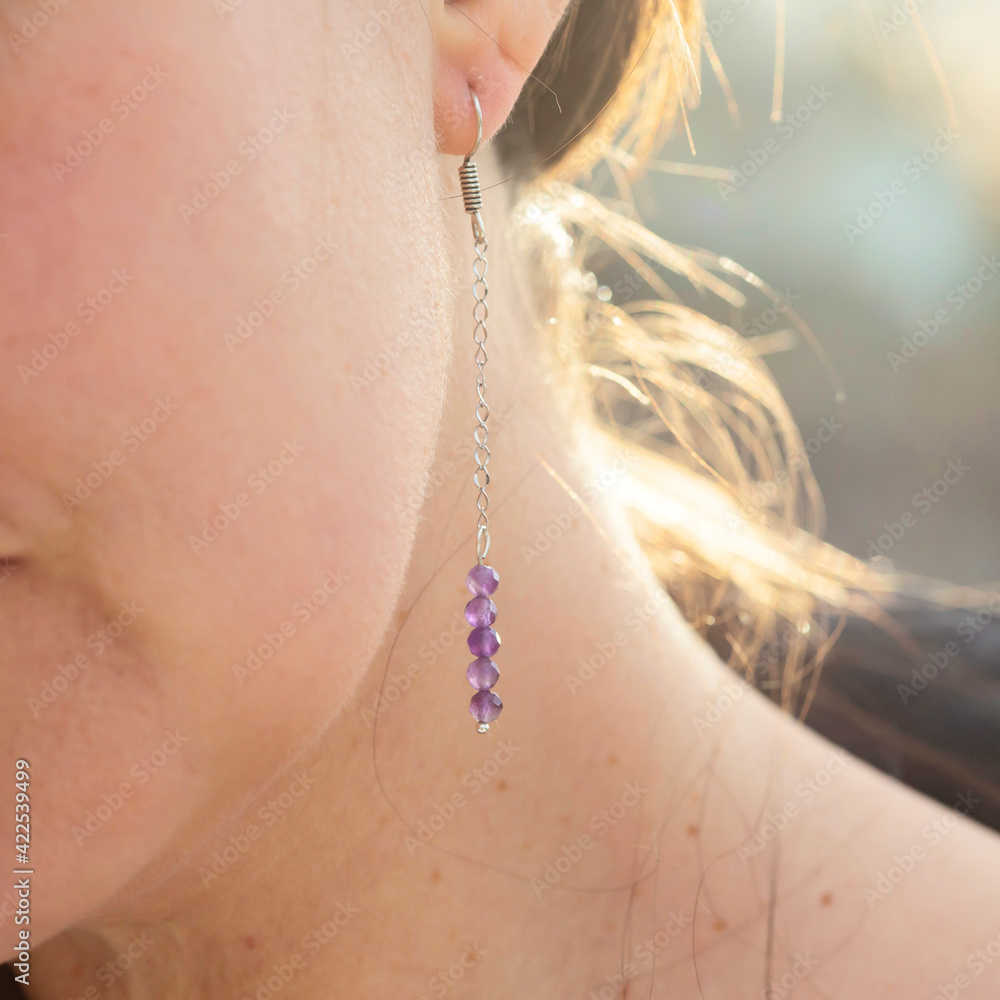 Female ear wearing long amethyst mineral stone earring Female ear wearing long amethyst mineral stone earring