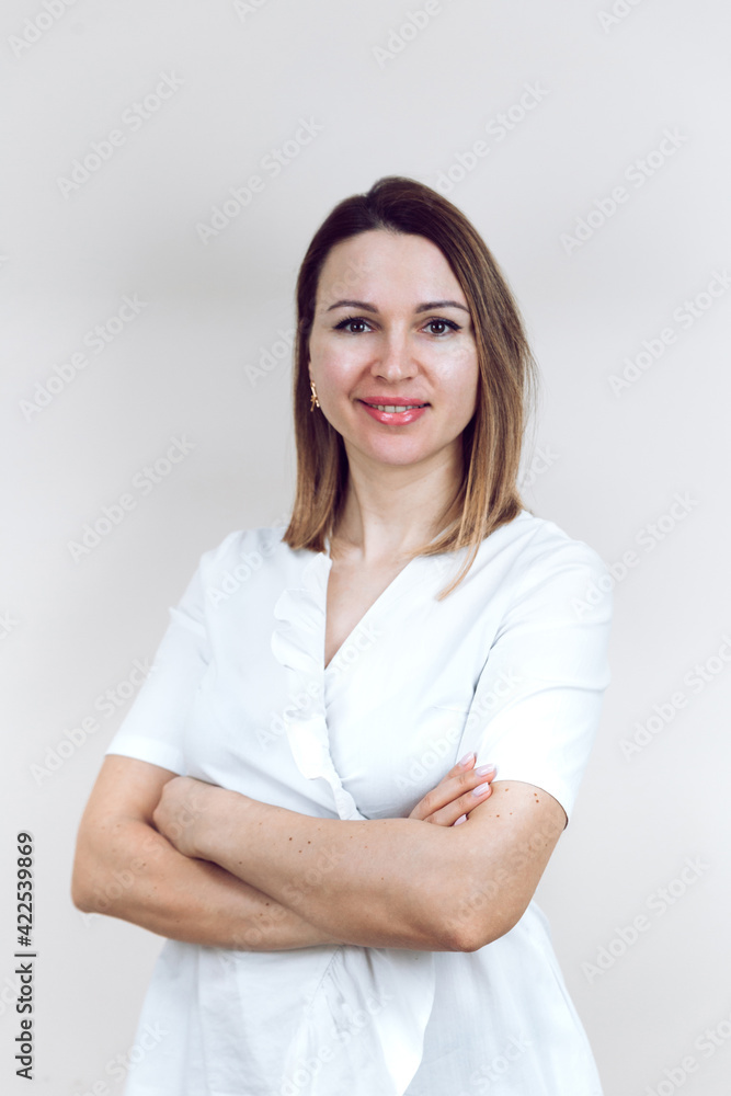 Beautiful young female doctor in a white medical gown, on an isolated white background. The beautician smiles into the camera, arms folded. With place for text or logo. Beautiful young female doctor in a white medical gown, on an isolated white background. The beautician smiles into the camera, arms folded. With place for text or logo.