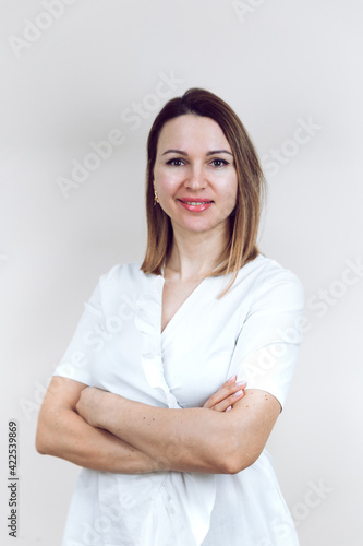 Beautiful young female doctor in a white medical gown, on an isolated white background. The beautician smiles into the camera, arms folded. With place for text or logo.