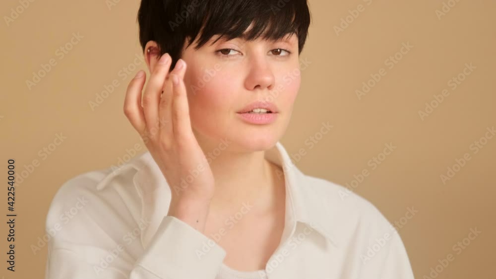 Woman apply moisturizing cream on face. Skin care, lifting facial creme and natural cosmetic product. Female with short haircut touches skin with hands rubbing anti aging lotion. Woman apply moisturizing cream on face. Skin care, lifting facial creme and natural cosmetic product. Female with short haircut touches skin with hands rubbing anti aging lotion.