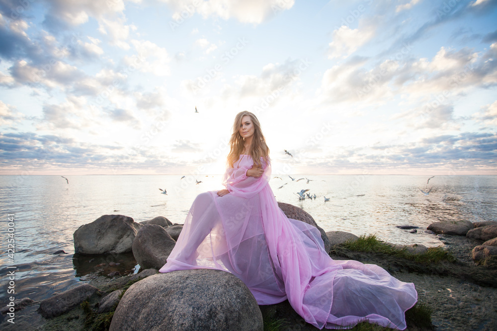 Fashionable young woman with blonde hair in pink silky dress against sky outdoor Fashionable young woman with blonde hair in pink silky dress against sky outdoor