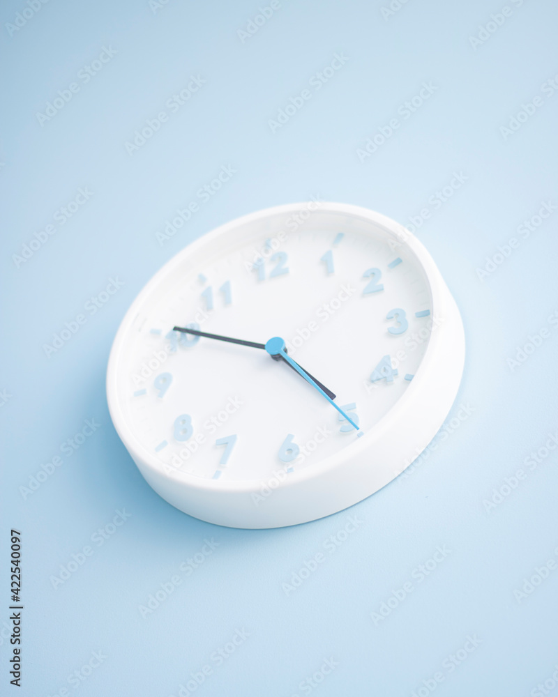 Minimalistic white wall clock on a blue background. Time concept. Vertical with copy space. Minimalistic white wall clock on a blue background. Time concept. Vertical with copy space.
