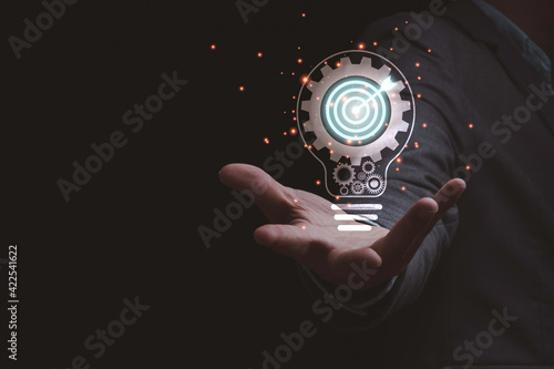Canvastavla Businessman holding virtual lightbulb which contain mechanical gear and target board, creative thinking idea for business achievement concept