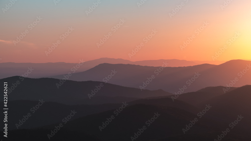 Fototapeta premium A panorama of a vibrant orange, yellow, blue sunset over the layers of the Appalachian Mountain range from Shenandoah National Park, Virginia, USA.