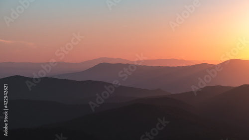 A panorama of a vibrant orange, yellow, blue sunset over the layers of the Appalachian Mountain range from Shenandoah National Park, Virginia, USA.