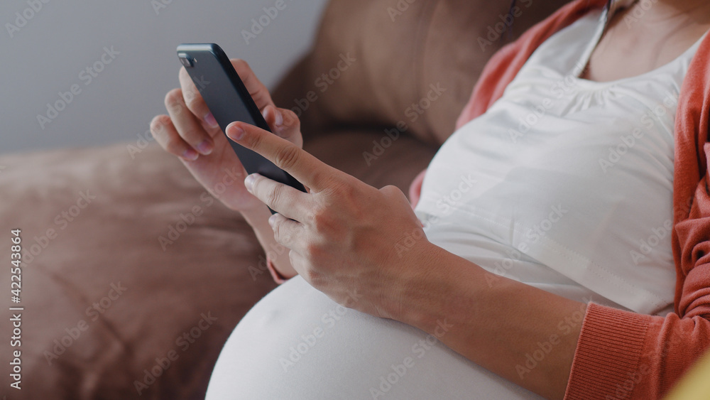 Young Asian Pregnant woman using mobile phone search pregnancy information. Mom feeling happy smiling positive and peaceful while take care her child lying on sofa in living room at home concept. Young Asian Pregnant woman using mobile phone search pregnancy information. Mom feeling happy smiling positive and peaceful while take care her child lying on sofa in living room at home concept.