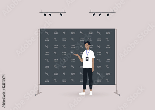 A young male character standing in front of a black press wall background covered with a logo pattern, a press conference event