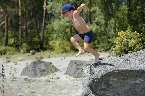 Happy child jumping from stone to sand on the beach at summer. Holidays and vacation season