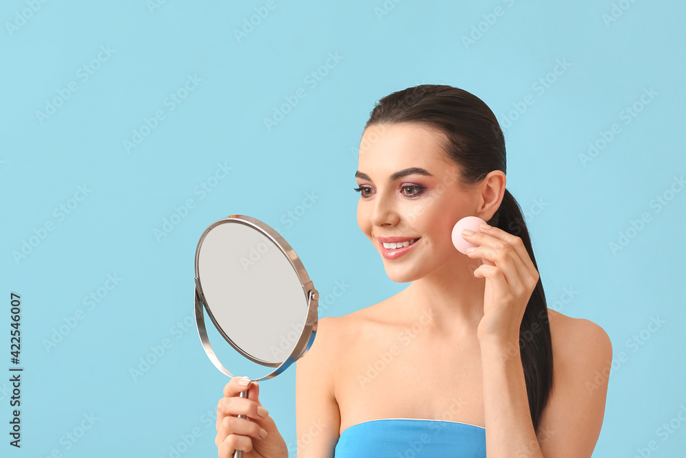Beautiful young woman with makeup sponge and mirror on color background Beautiful young woman with makeup sponge and mirror on color background