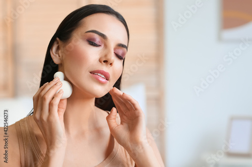 Beautiful young woman applying makeup at home