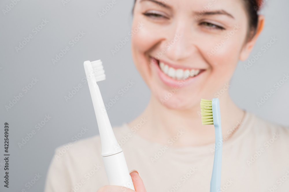 Happy woman compares a toothbrush with an electric one. The girl chooses oral hygiene products Happy woman compares a toothbrush with an electric one. The girl chooses oral hygiene products