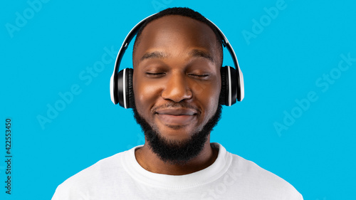 African American Man Wearing Headphones Listening To Music, Blue Background