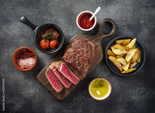 Sliced grilled meat steak New York Striploin or club steak with sauce and potato on wooden board on grey background. Flat lay, top view.