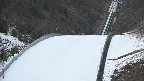 Winter ski jump ramp in Kranj, Slovenia. Jumper runs down to generate sufficient speed before reaching the jump. Person glide down on tracks along the in-run. Static shot, slow motion
