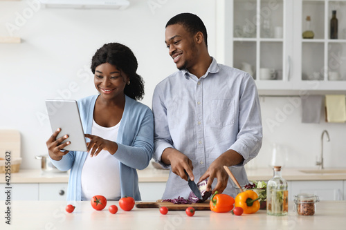 Smiling black pregnant couple using digital tablet in kitchen