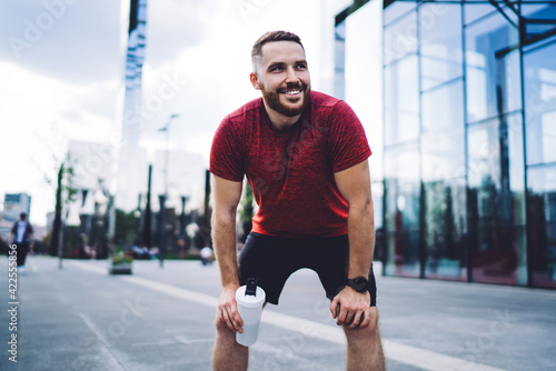 Cheerful sportsman resting after workout on pavement