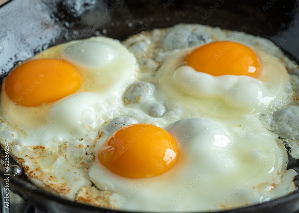 Keto meal eggs frying on hot cast iron frying pan, three fried yellow yolk, ketogenic diet, fat protein breakfast. Macro side view of cooking in the kitchen home interior, authentic lifestyle Keto meal eggs frying on hot cast iron frying pan, three fried yellow yolk, ketogenic diet, fat protein breakfast. Macro side view of cooking in the kitchen home interior, authentic lifestyle