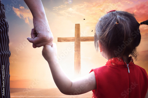 Foto Child's hand holding mother's finger on blurred The cross of jesus christ background