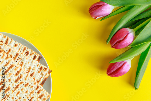 Traditional Jewish food matzo bread and pink tulips on a yellow background. Happy Passover. Religious spring holiday Pesach. Copy space. #422557432