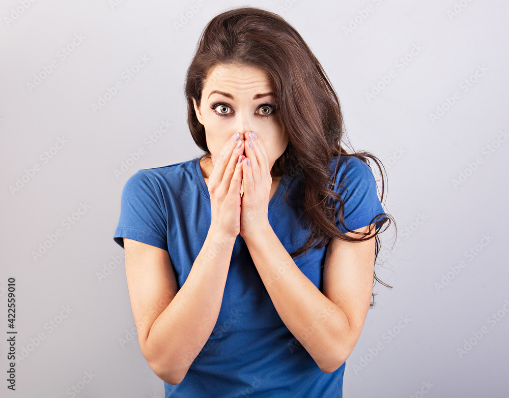 adult; amazed; Pretty shocked woman covering the face the hands with wide opened eyes in casual t-shirt dress looks scared. Studio shot adult; amazed; Pretty shocked woman covering the face the hands with wide opened eyes in casual t-shirt dress looks scared. Studio shot