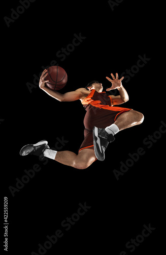 Young professional basketball player in action, motion isolated on black background, look from the bottom. Concept of sport, movement, energy and dynamic. © master1305