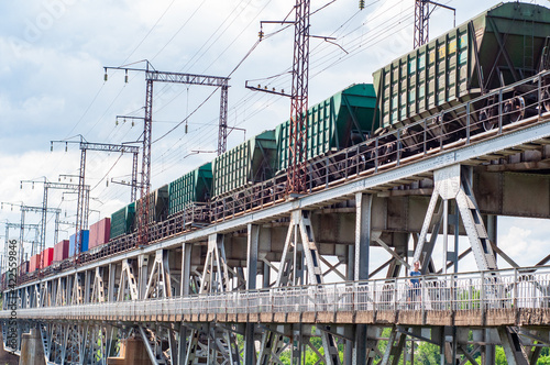 Long railway train on iron bridge over river, freight wagons.