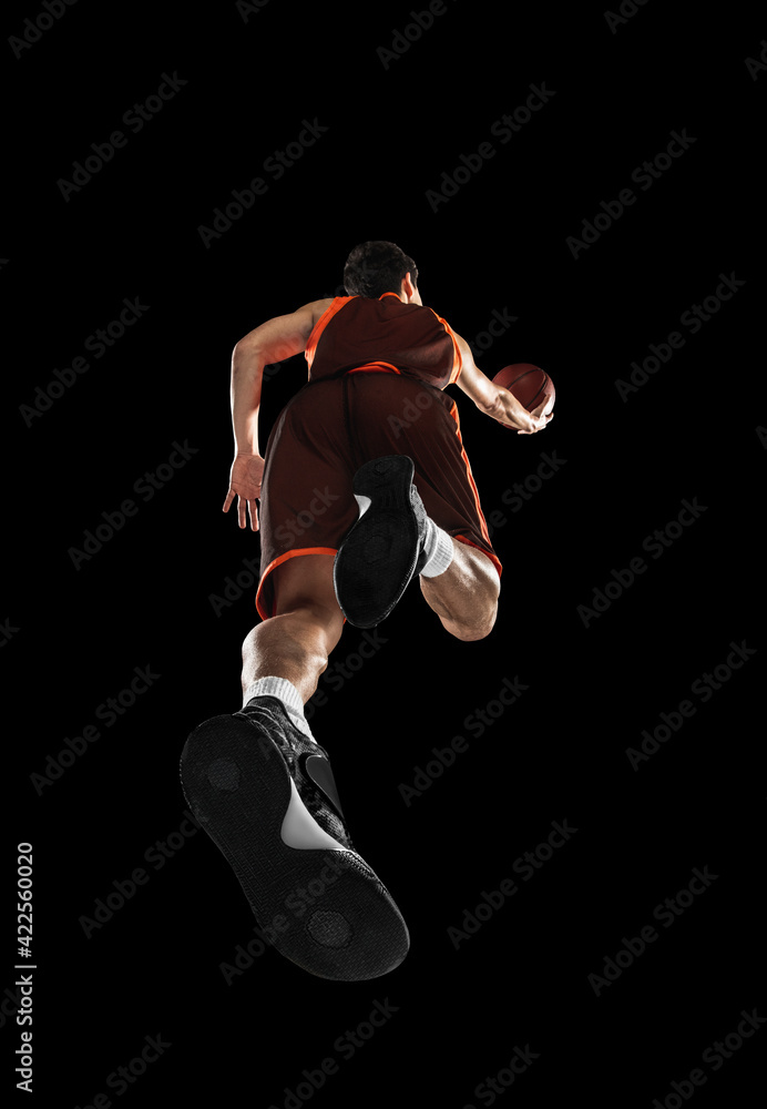 Young professional basketball player in action, motion isolated on black background, look from the bottom. Concept of sport, movement, energy and dynamic.
