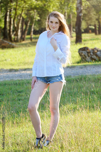 Beautiful girl wears hot pants and blouse and poses in the park on a sunny summer day