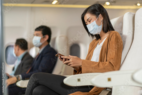 Passengers wearing masks and smartphones in the plane during the flight. New normal concept. photo