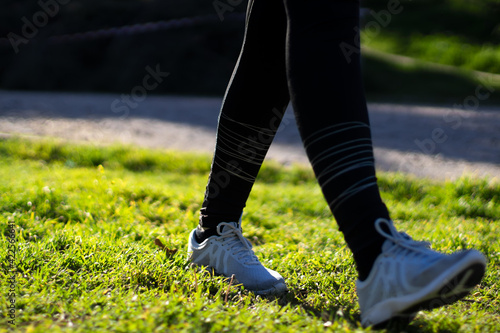 woman runner walking on the grass field in a park in the morning. Close-up on shoe