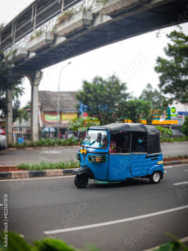 A bajaj car crosses the middle of Jakarta Indonesia's road, above which there is a bridge for people to cross safely