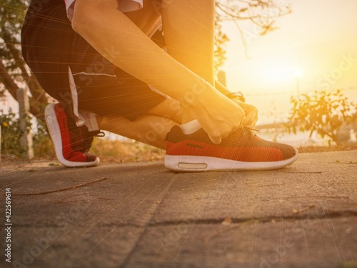 The lady wore black and red shoes who wearing his shoelaces before jogging in the sunset at the park. In order to prepare the healthy to be ready before competing in Marathon