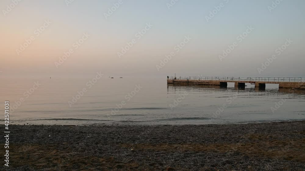 San Simon bay, Slovenia: concrete pier in winter. Calm waves hitting pebble beach at sunset. Beautiful colors at golden hour. Static shot, real time, wide angle San Simon bay, Slovenia: concrete pier in winter. Calm waves hitting pebble beach at sunset. Beautiful colors at golden hour. Static shot, real time, wide angle