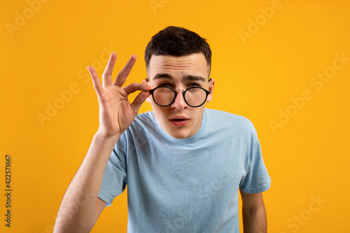 Young Caucasian man in glasses being skeptical, looking suspicious, having some doubt on orange studio background